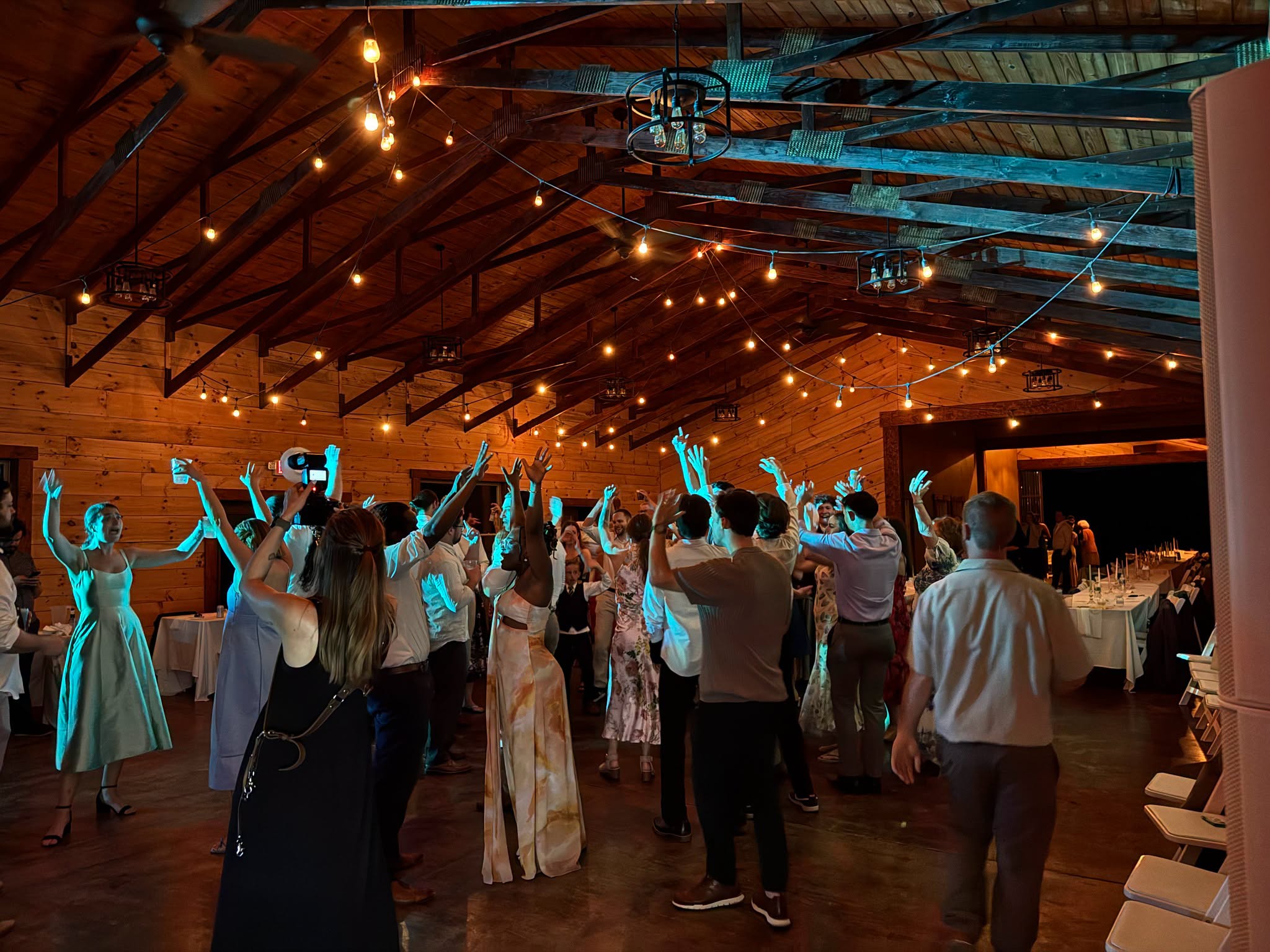Guests dancing with their hands in the air in a rustic timber barn venue with string lights